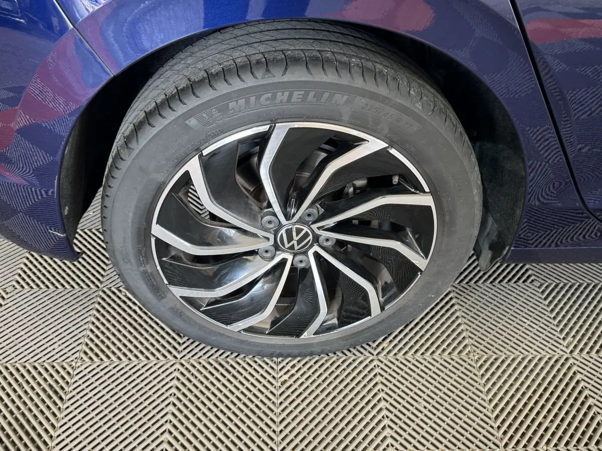 Gros plan sur la roue avant gauche avec jante alliage noire et argentée du Volkswagen Golf bleu 2021.