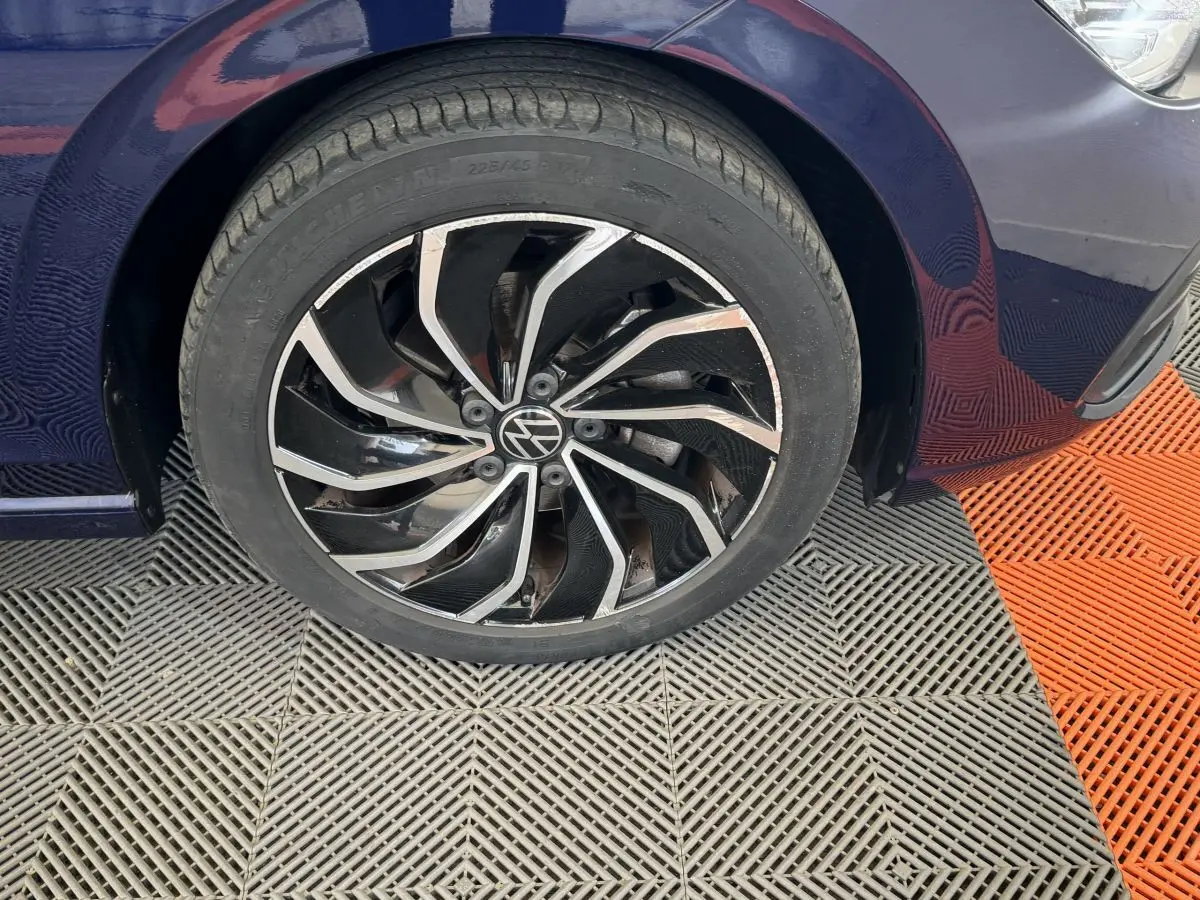 Gros plan sur la roue avant gauche d'une Volkswagen Golf bleu foncé avec jante alliage noire et argentée.