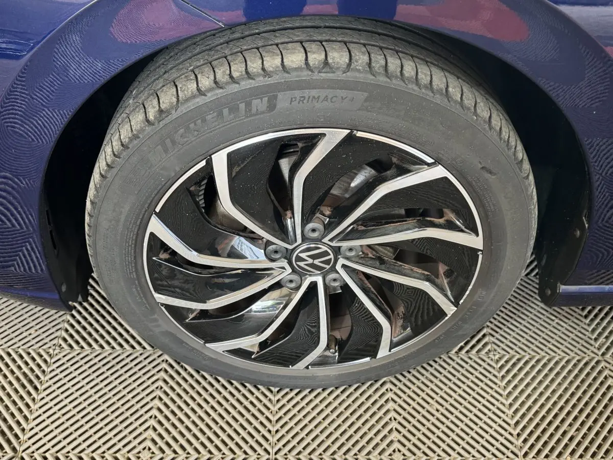 Gros plan sur la roue avant droite bleu métallisé d'une Volkswagen Golf avec jante alliage noire et argentée.