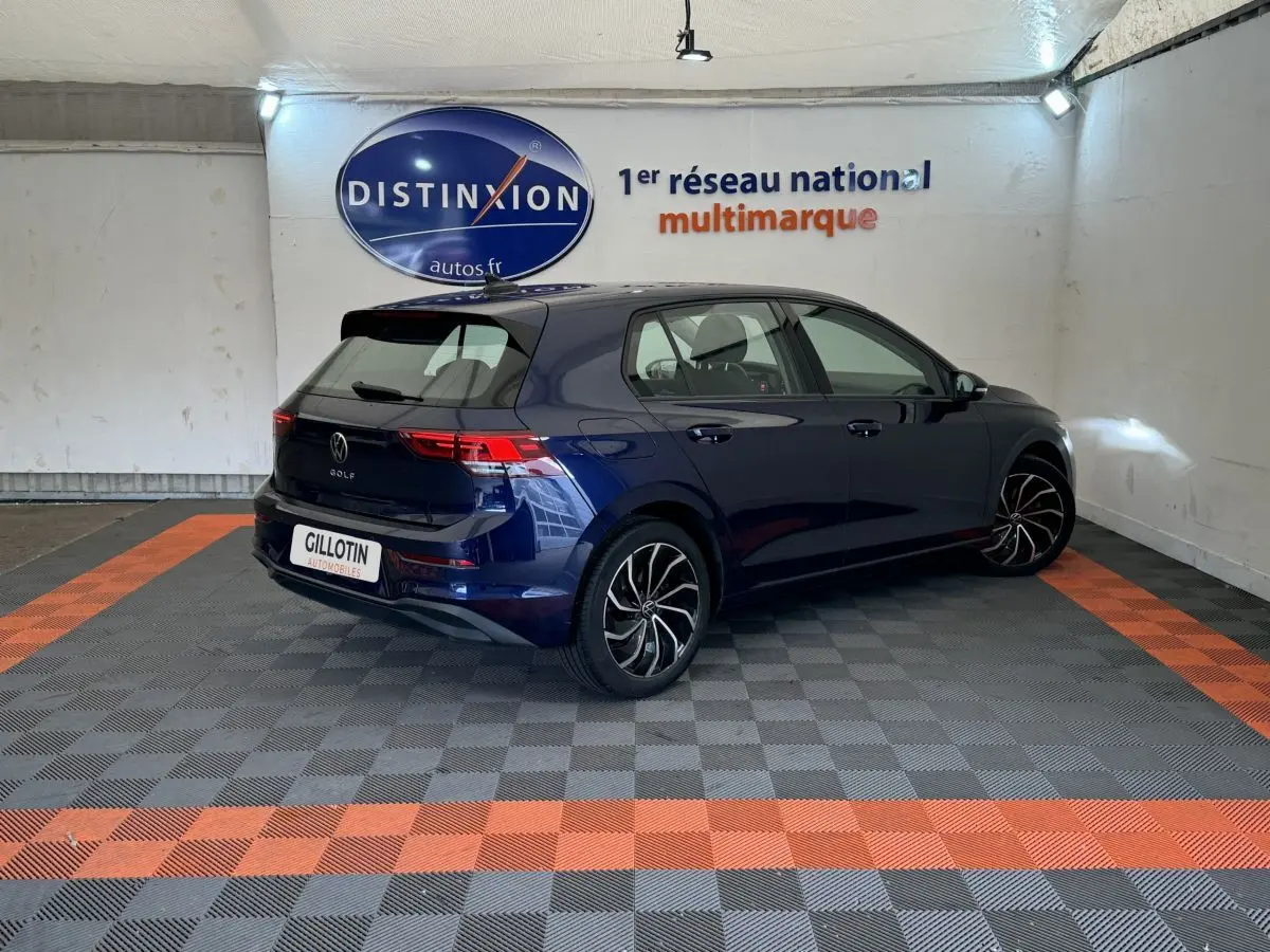 Volkswagen Golf bleu vue 3/4 arrière droit dans un showroom avec jantes noires et rouges.
