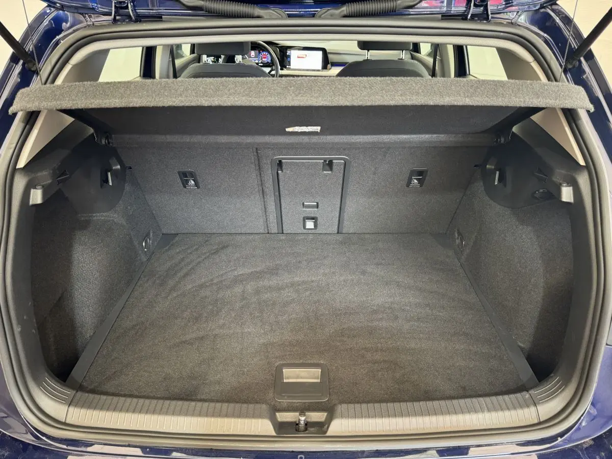 Coffre ouvert d'une Volkswagen Golf bleu 2021, vue de l'arrière avec tablette cache-bagages et intérieur noir.