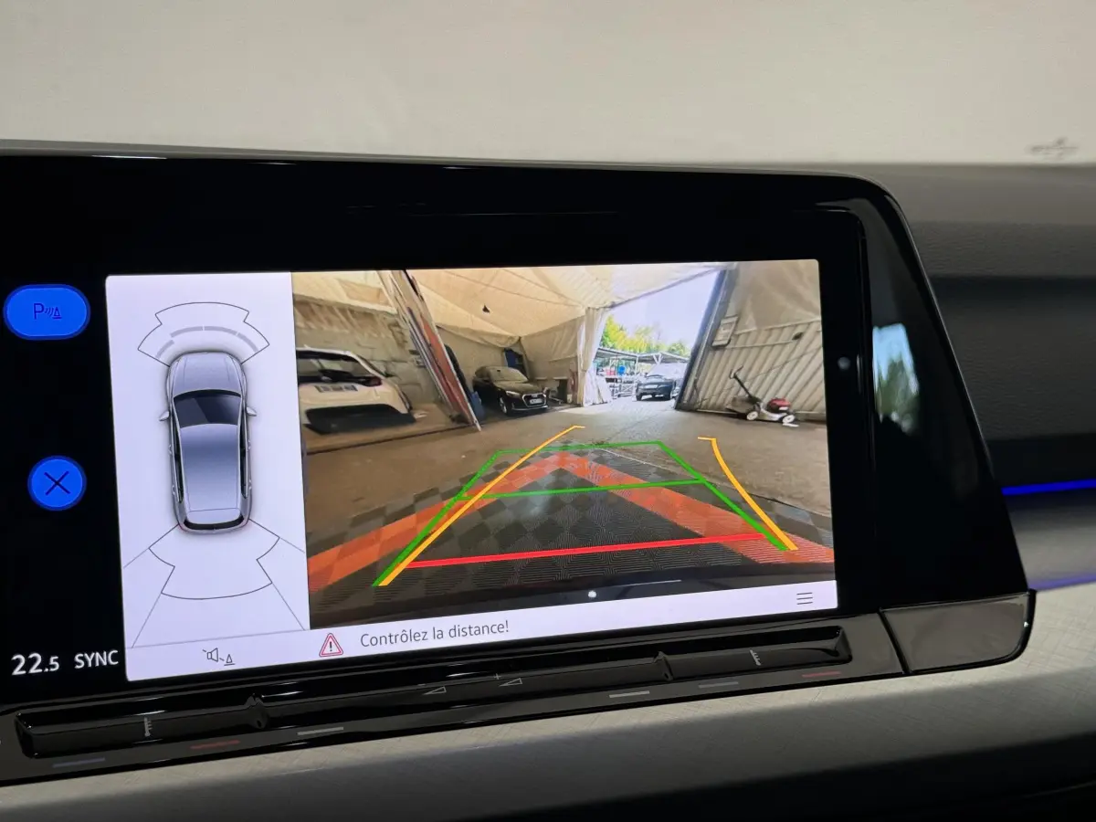 Écran tactile intérieur affichant la caméra de recul et les capteurs de distance d'une Volkswagen Golf bleue.