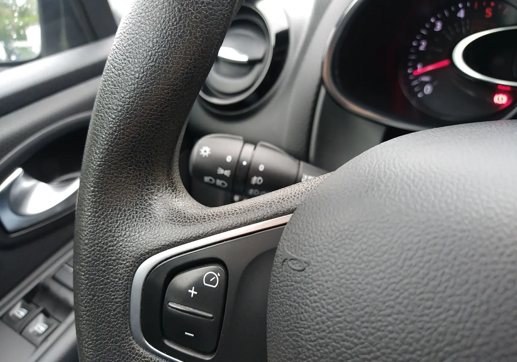 Gros plan sur le volant et la commande de régulateur de vitesse d'une Renault Clio IV Société blanche, tableau de bord partiellement visible.