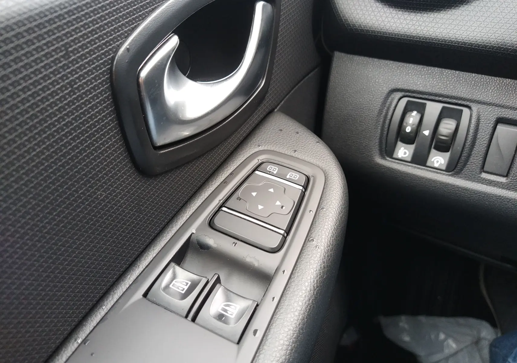 Gros plan sur la commande des vitres électriques et la poignée intérieure côté gauche d'une Renault Clio IV Société blanche.