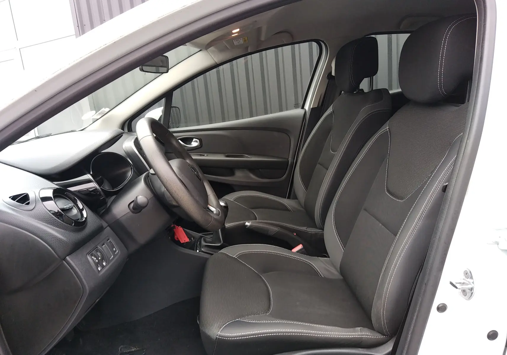 Intérieur côté conducteur d'une Renault Clio IV Société blanche, sièges tissu noir avec surpiqûres blanches visibles.