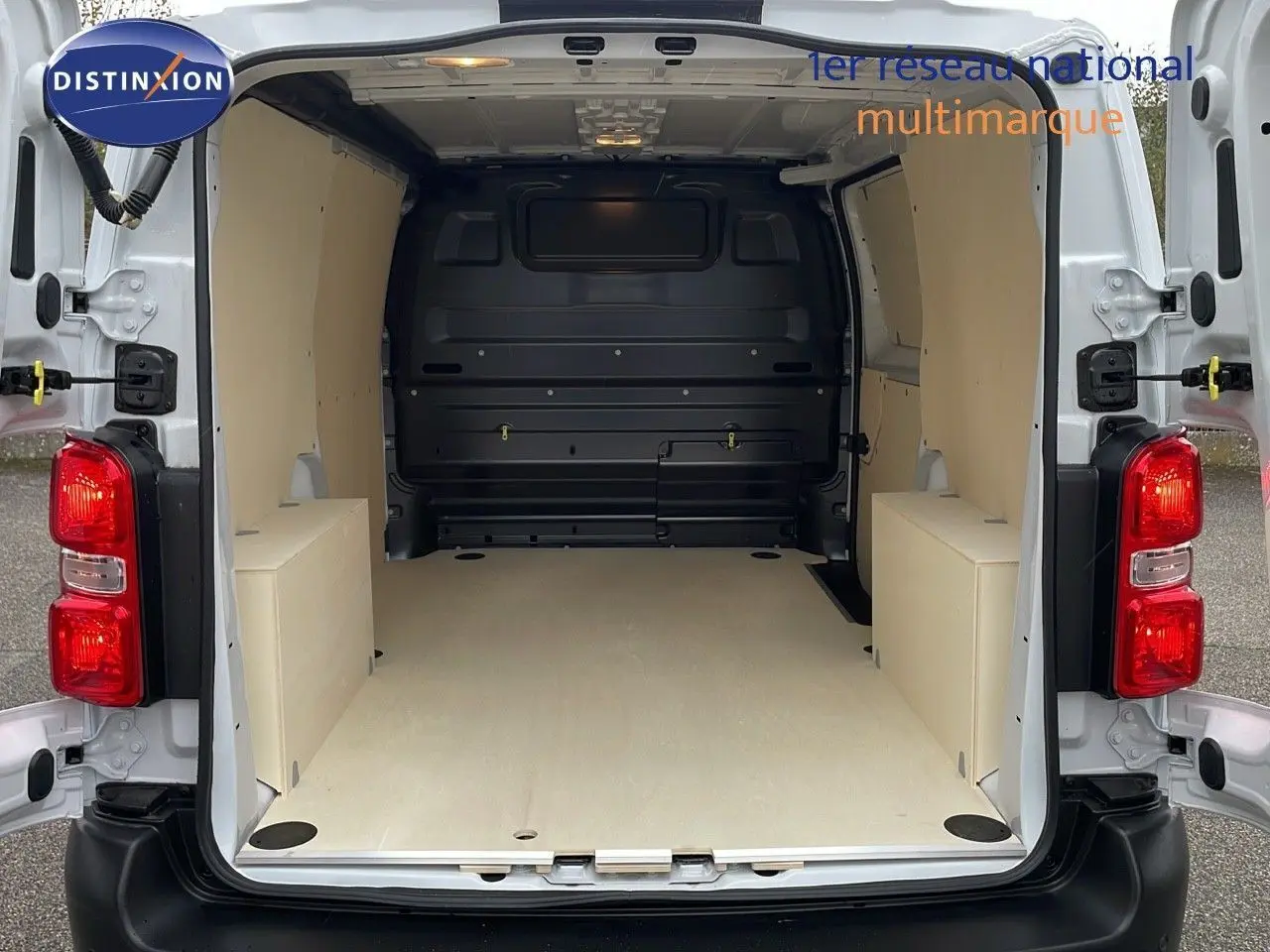 Vue arrière du Peugeot Expert Fourgon blanc 2025 avec portes ouvertes, montrant l'espace de chargement aménagé en bois clair.