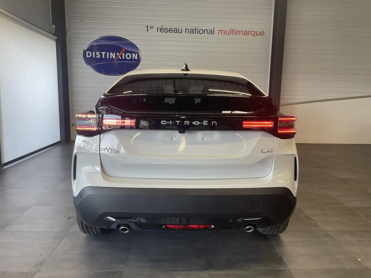 Vue arrière d'une Citroën C4 blanche métallisée avec feux LED allumés et bande noire distinctive sur le coffre.