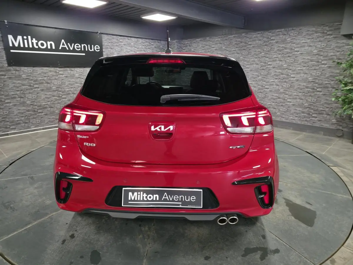 Vue arrière d'une KIA Rio GT Line rouge métallisée avec double sortie d'échappement et feux LED allumés.