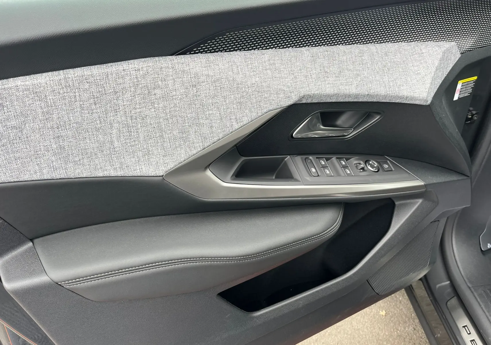 Gros plan sur la porte côté gauche du Peugeot 3008 gris titane, avec garniture tissu gris et commandes électriques intégrées.