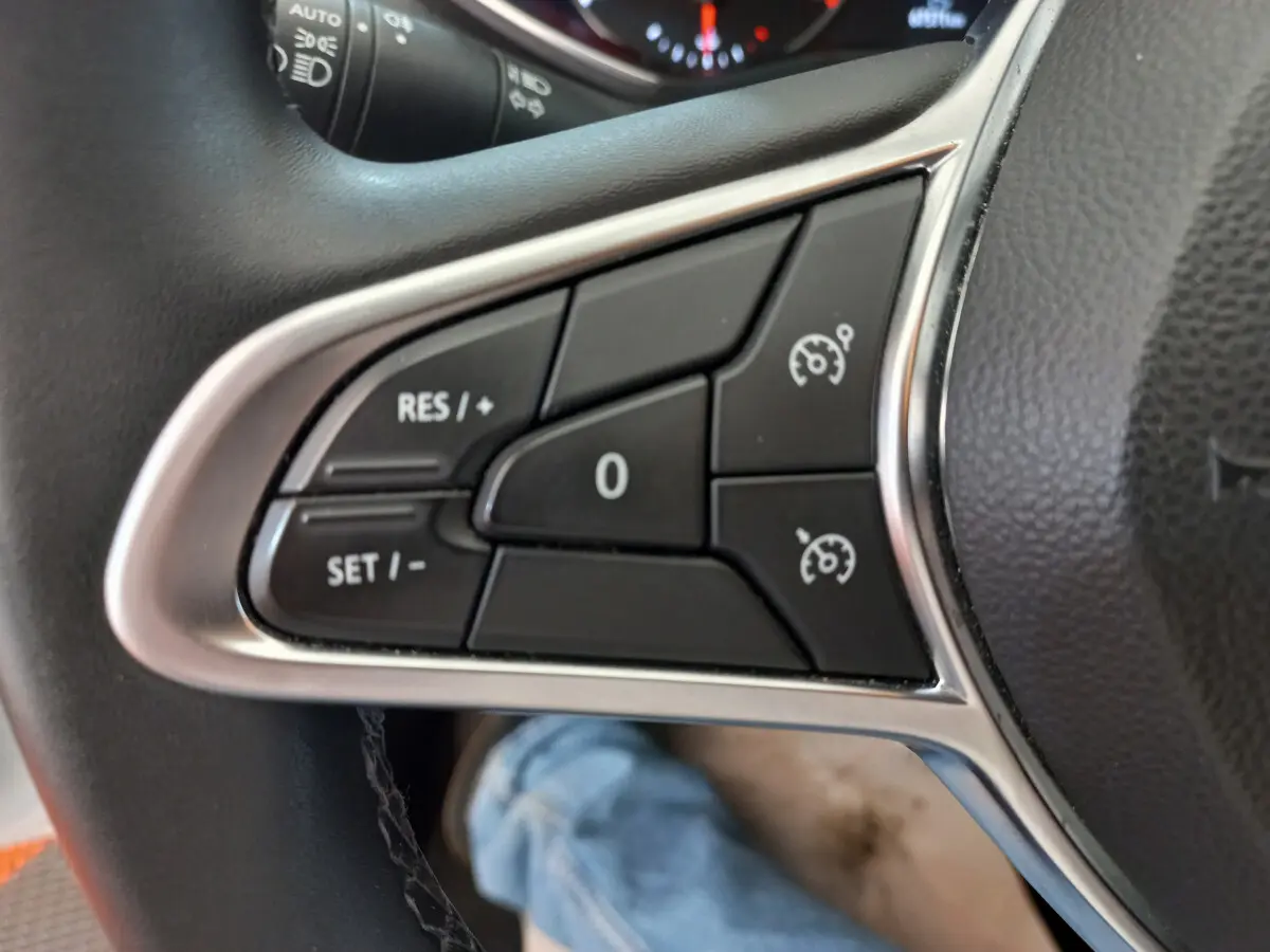 Gros plan sur les commandes de régulateur de vitesse au volant cuir synthétique d'une Renault Clio Business blanche 2021.