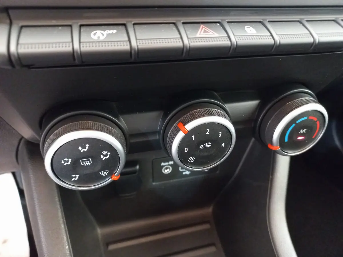 Gros plan sur les commandes de climatisation de la Renault Clio Business blanche, avec réglages rotatifs noirs et indicateurs rouges.