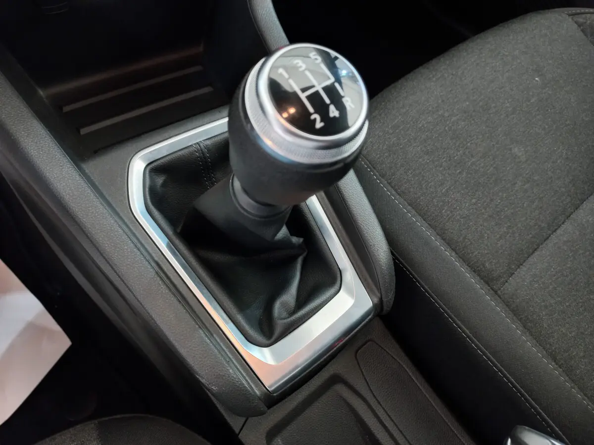 Gros plan sur le levier de vitesses manuel noir et argenté de la Renault Clio Business blanche, avec siège tissu gris à côté.