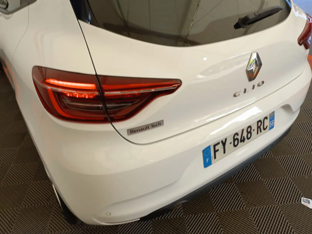 Vue 3/4 arrière droite d'une Renault Clio blanche avec feux LED et badge Renault Tech visible sur le coffre.