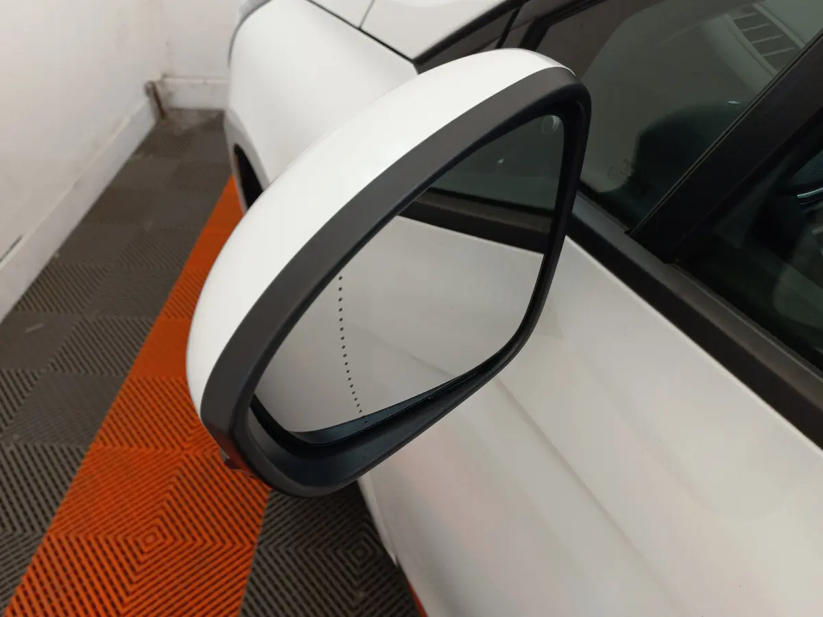 Rétroviseur côté gauche blanc de la Renault Clio Business 2021, vue rapprochée sur fond de sol gris et orange.