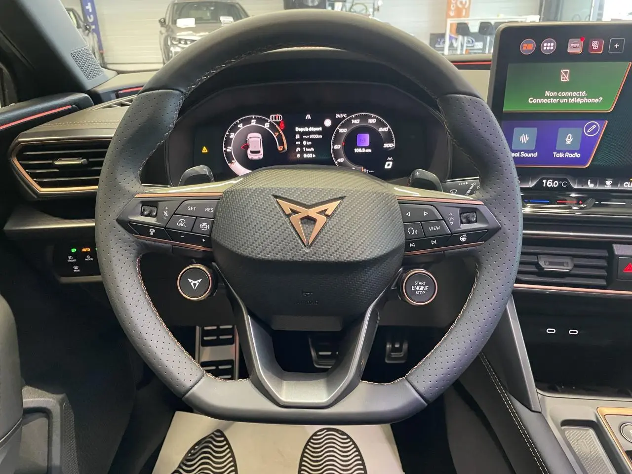 Volant CUPRA en cuir perforé avec logo cuivré, tableau de bord digital et écran tactile central dans l'habitacle noir.