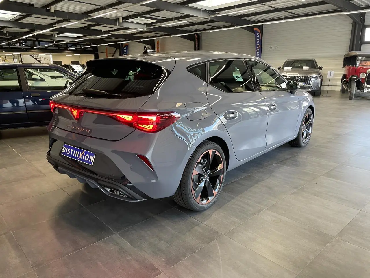 Vue 3/4 arrière droite d'une CUPRA Leon gris magnétique avec jantes cuivrées et feux arrière Tri-LED allumés.