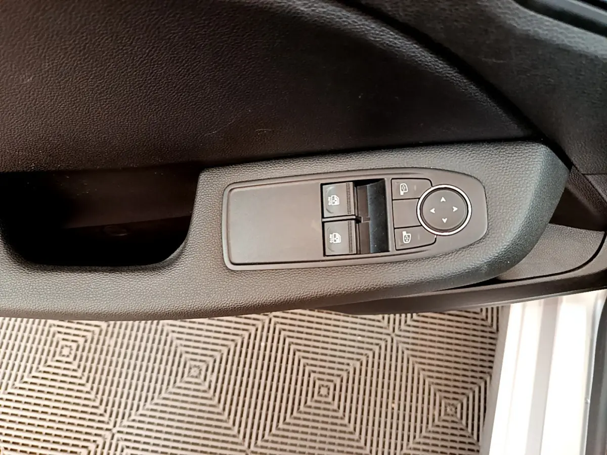 Gros plan sur la commande des vitres et rétroviseurs côté conducteur d'une Renault Clio Business E-Tech gris clair.