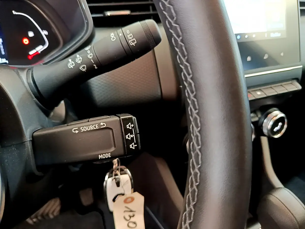 Gros plan sur le volant cuir noir et la commande multimédia à gauche dans l'habitacle d'une Renault Clio gris clair hybride.