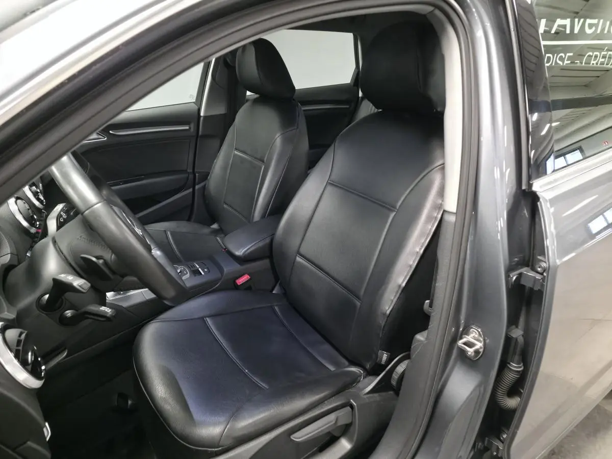 Vue intérieure côté conducteur de l'Audi A3 Sportback gris, sièges en similicuir noir et tableau de bord visible.