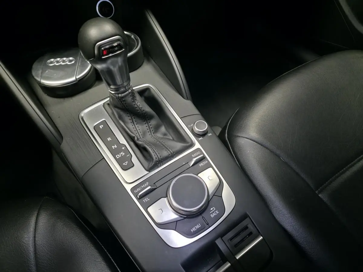 Gros plan sur la console centrale noire de l'Audi A3 Sportback, mettant en valeur le levier de vitesses automatique et les commandes multimédia.