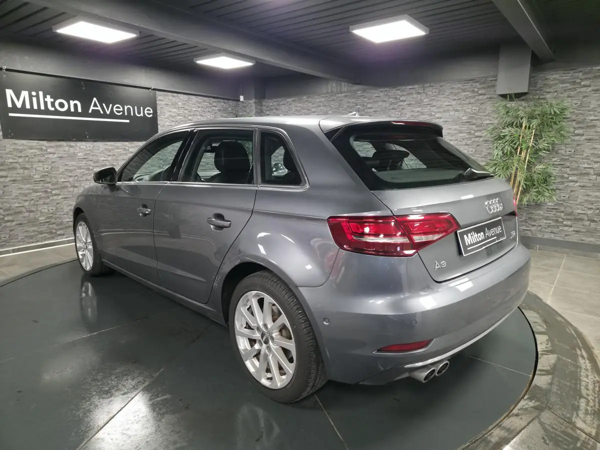 Audi A3 Sportback gris métallisé vue 3/4 arrière droit avec jantes aluminium 17 pouces en intérieur showroom