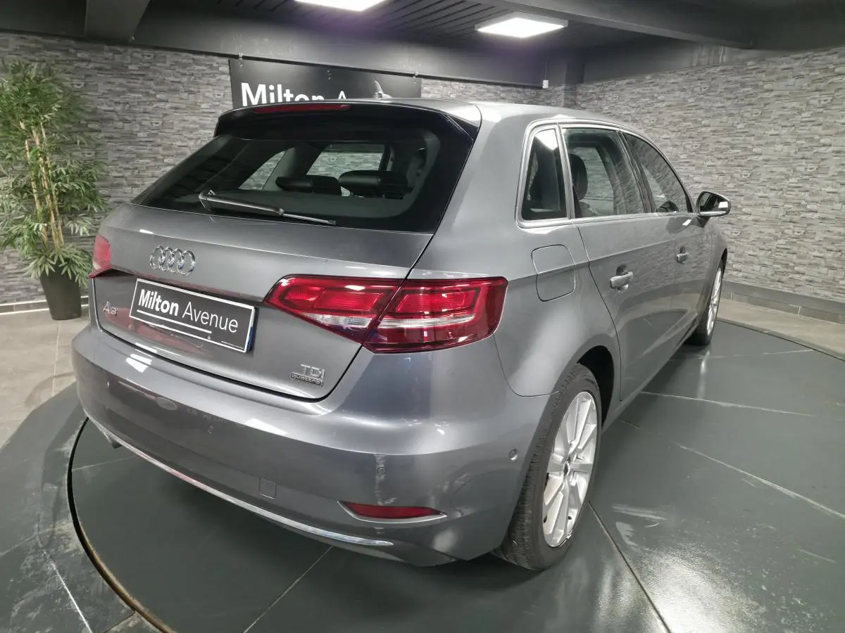 Audi A3 Sportback gris vue 3/4 arrière droit dans un showroom avec jantes aluminium 17 pouces.