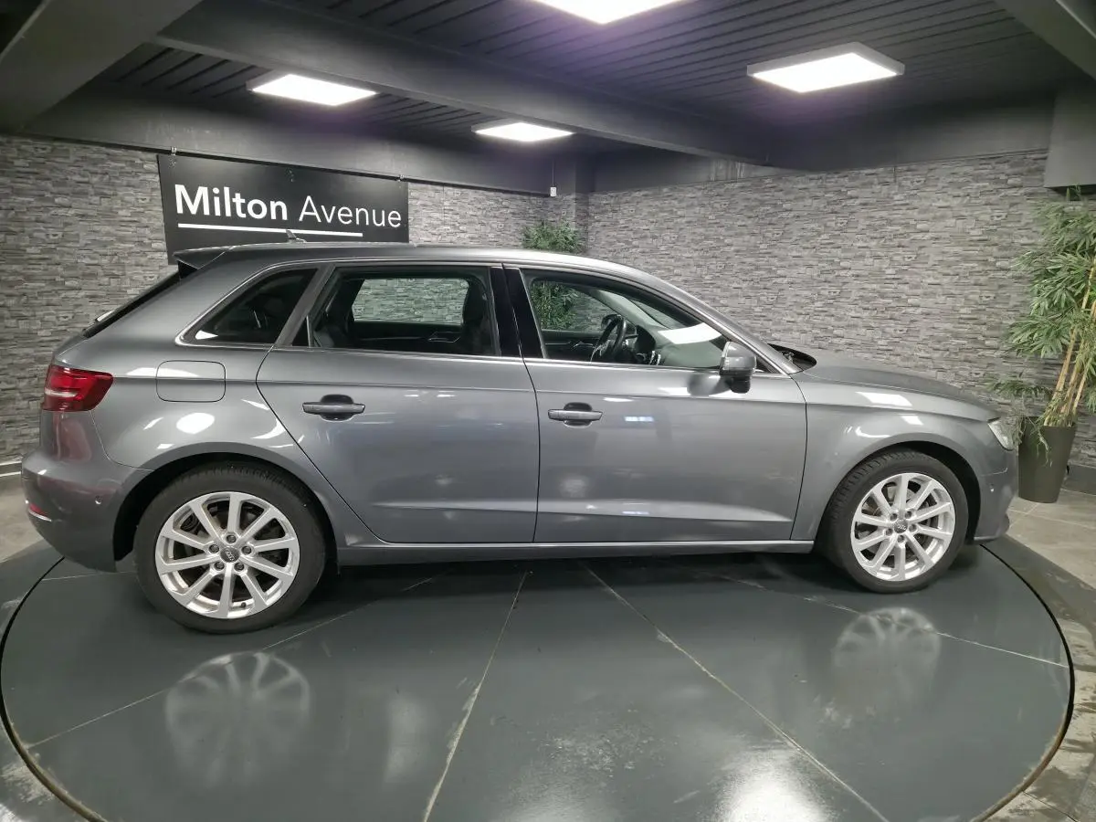Profil côté gauche d'une Audi A3 Sportback gris métallisé 2017 dans un showroom avec jantes aluminium 17 pouces.
