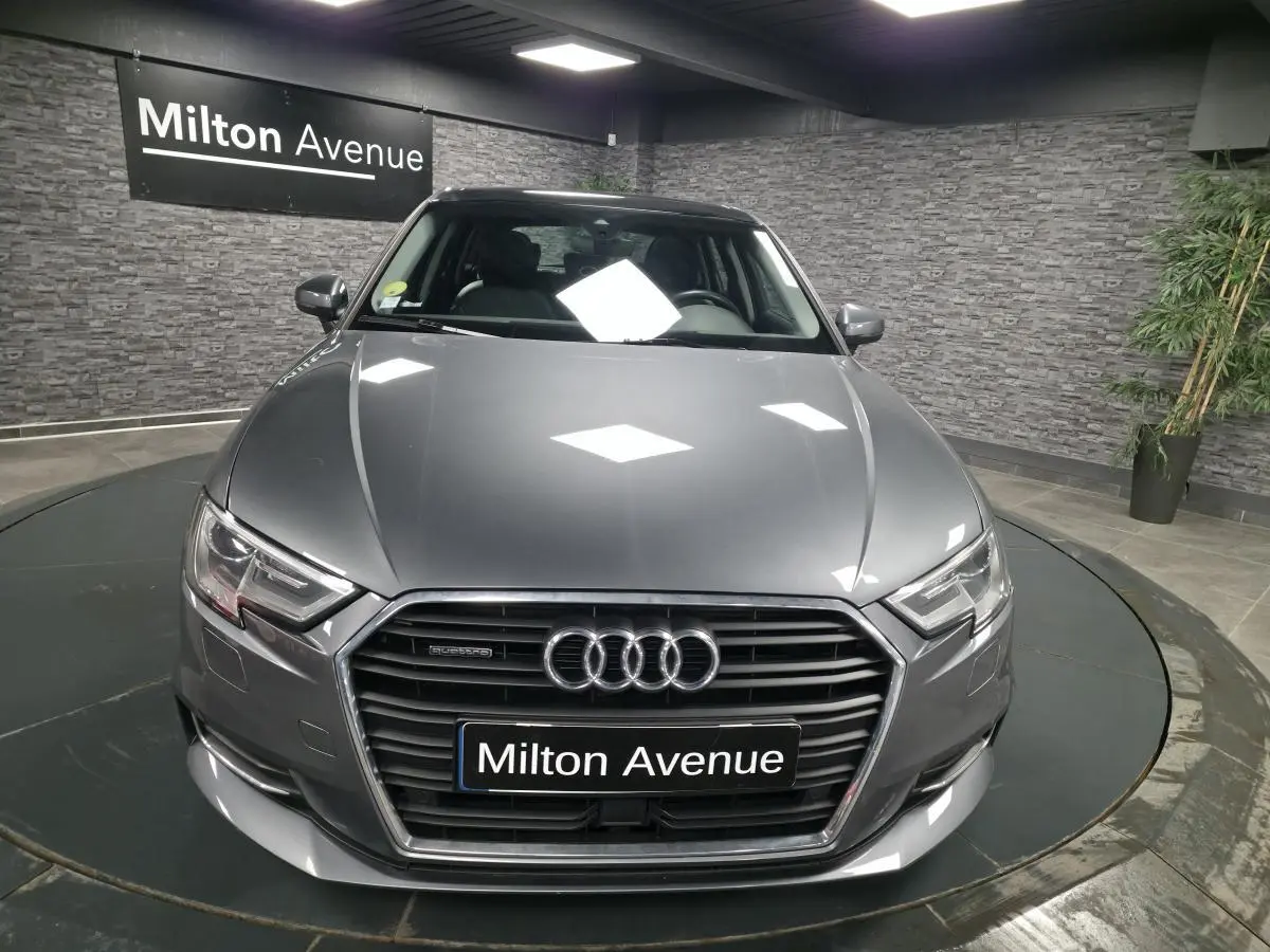 Audi A3 Sportback gris vue de face en intérieur avec calandre hexagonale et logo quatre anneaux lumineux.