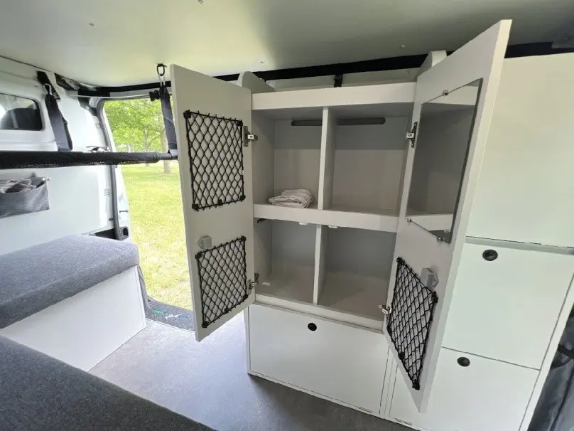 Vue intérieure du fourgon Renault Trafic gris, montrant un meuble de rangement blanc ouvert avec filets noirs sur les portes.