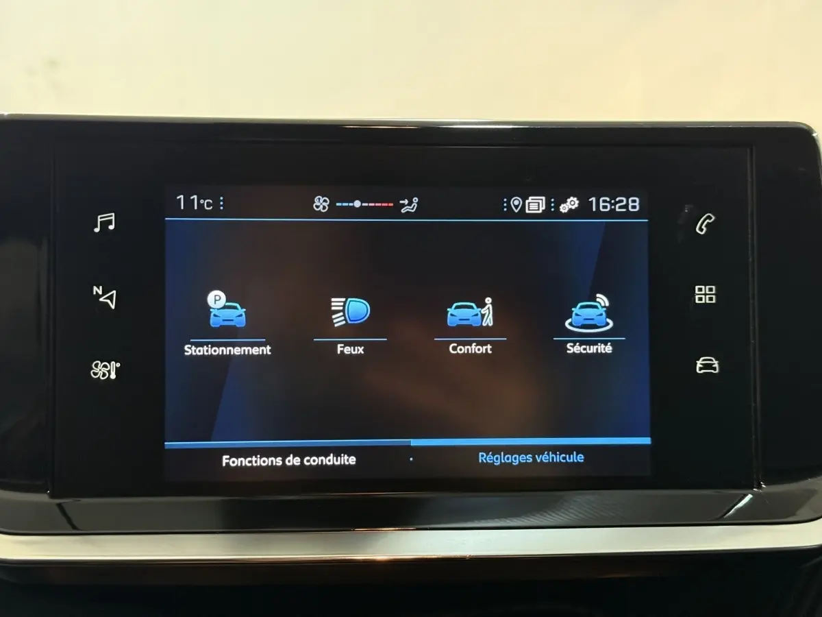 Écran tactile central du tableau de bord de la Peugeot 208 blanc, affichant les réglages de conduite et sécurité.