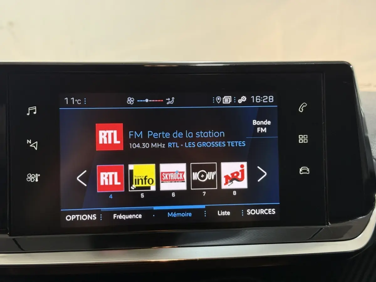 Écran tactile central de la Peugeot 208 blanc, affichant les stations radio FM avec interface moderne.