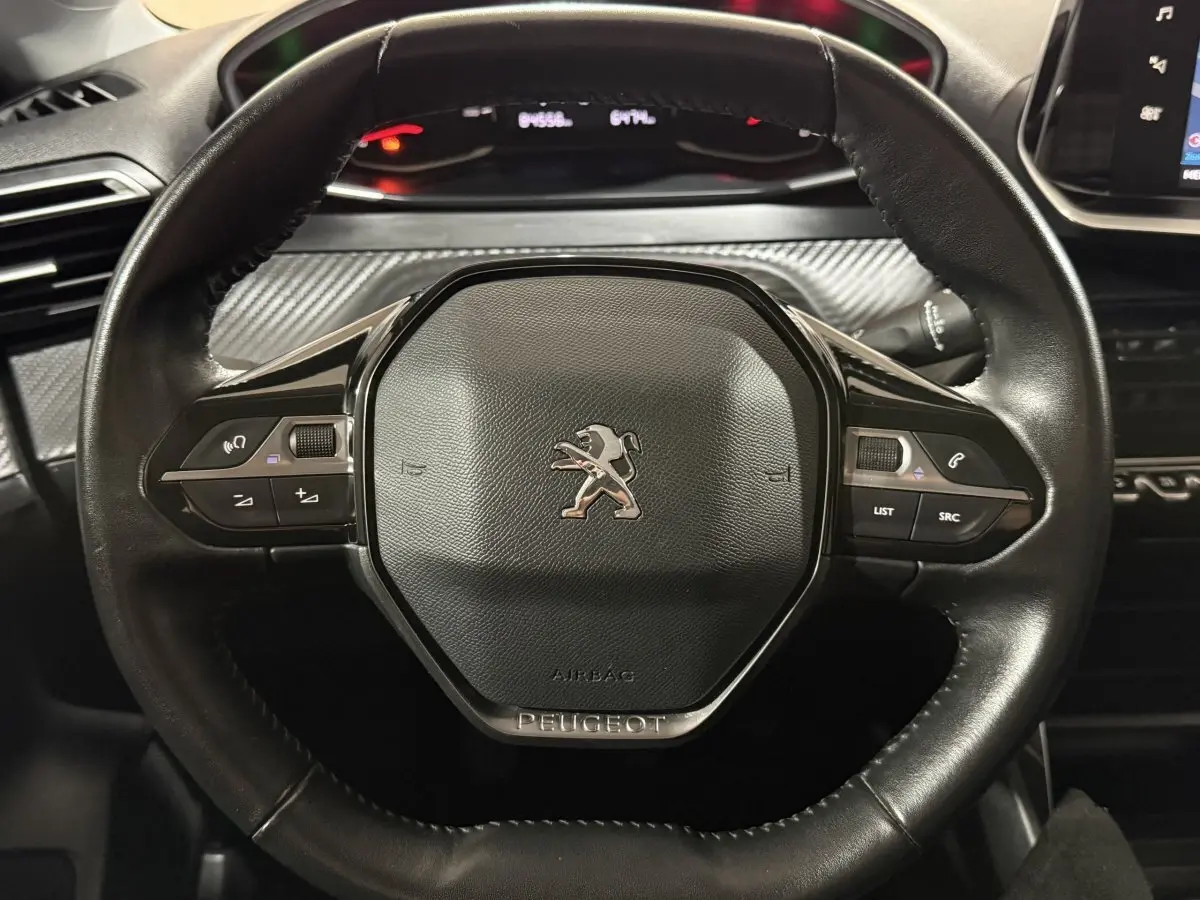 Volant noir de Peugeot 208 1.5 BlueHDi 2021 vu de face avec commandes intégrées et tableau de bord en arrière-plan.