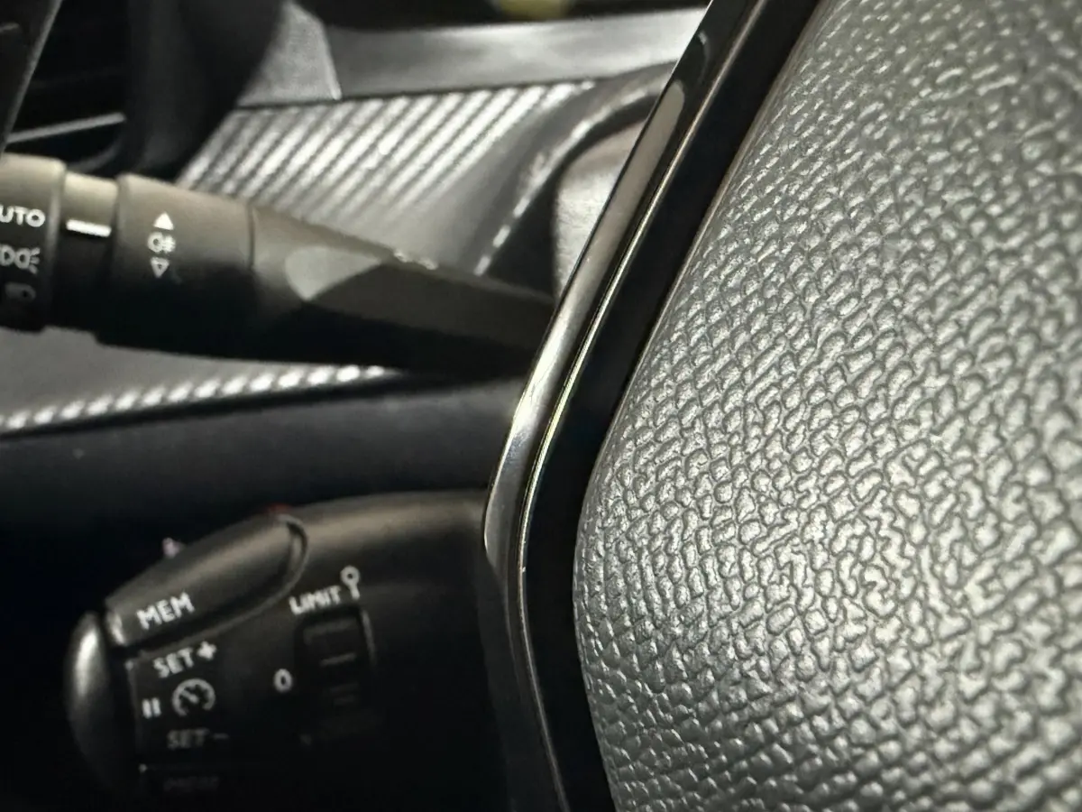 Gros plan sur le volant noir texturé et la commande de régulateur de vitesse d'une Peugeot 208 blanche, intérieur côté conducteur.
