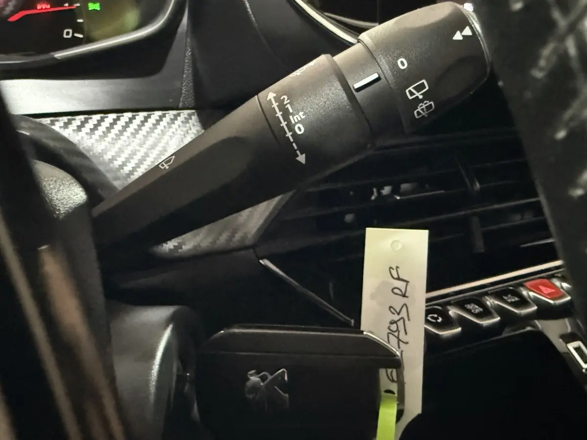 Gros plan sur la commande d’essuie-glace et la console centrale noire du tableau de bord d’une Peugeot 208 blanche.