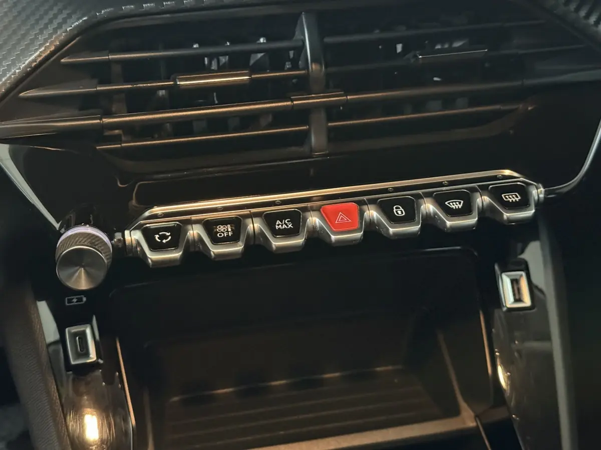 Gros plan sur la console centrale noire de la Peugeot 208 avec rangée de boutons chromés et USB visible.