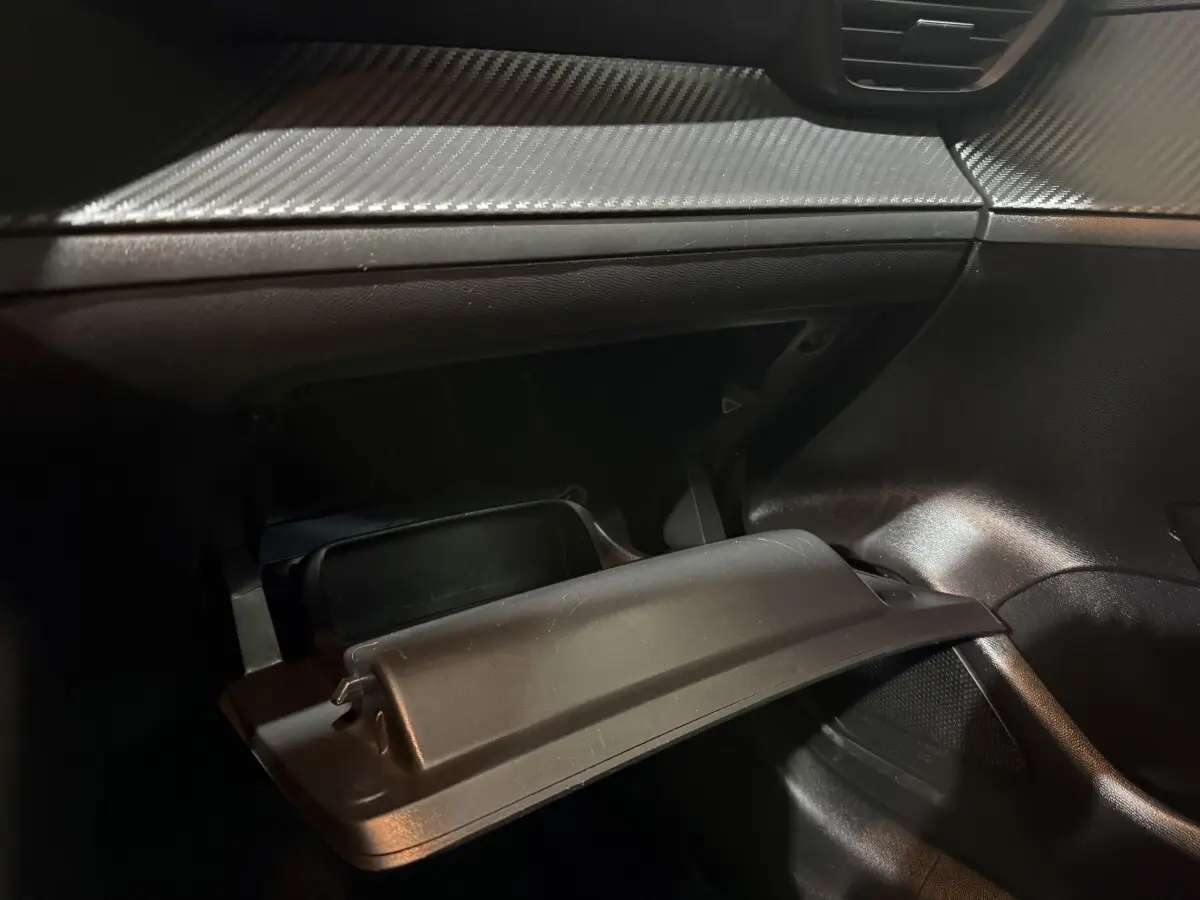 Gros plan de la boîte à gants ouverte côté passager dans l’habitacle noir de la Peugeot 208 blanche.