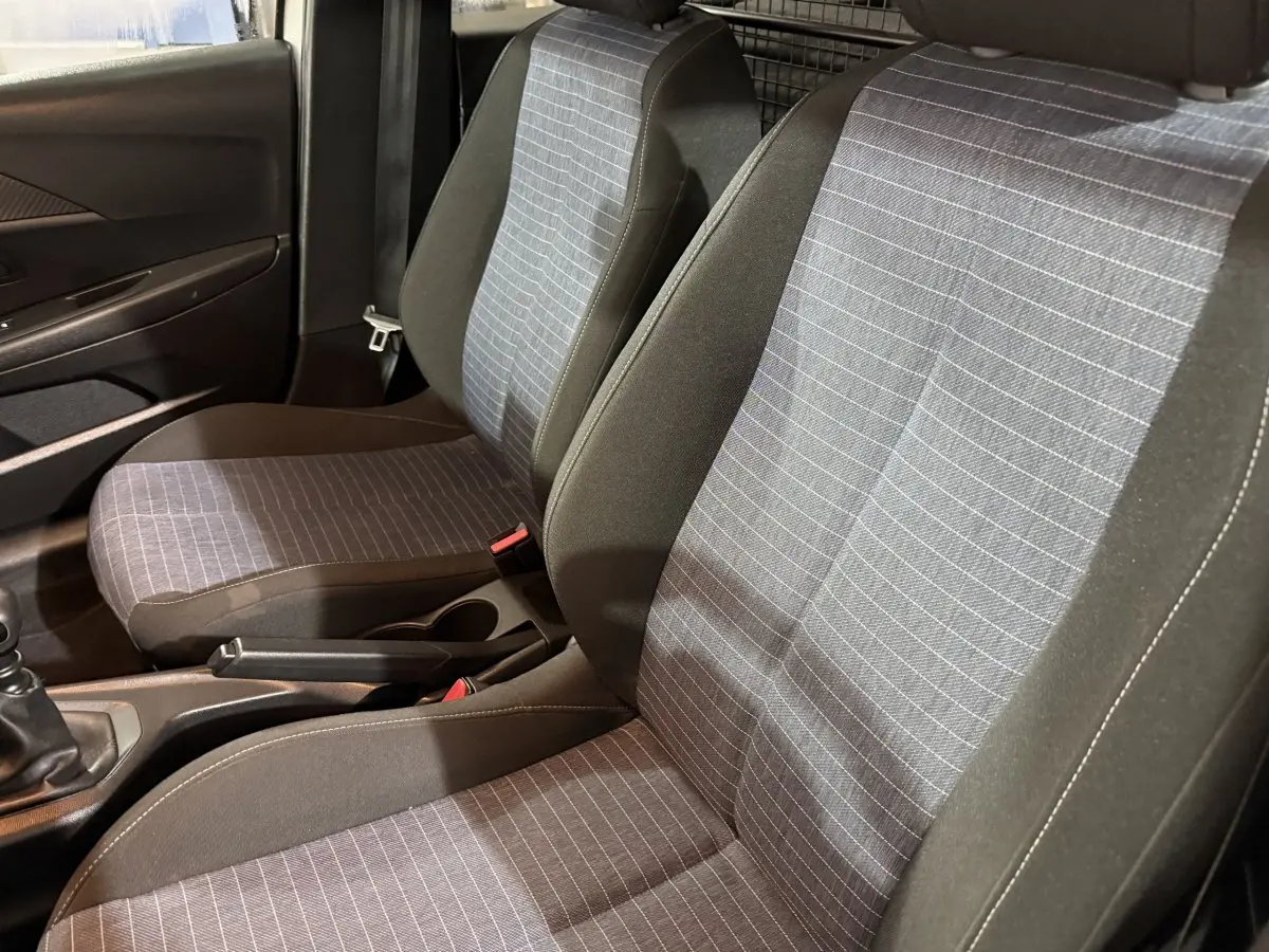 Vue intérieure rapprochée des sièges avant gris à motifs rayés de la Peugeot 208 1.5 BlueHDi 2021 avec cloison métallique arrière.