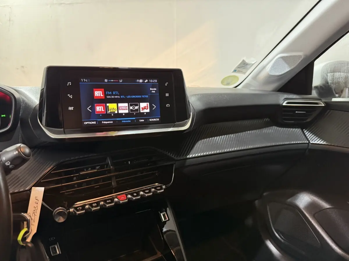 Vue intérieure côté passager du tableau de bord noir de la Peugeot 208 avec écran tactile central affichant une radio FM.