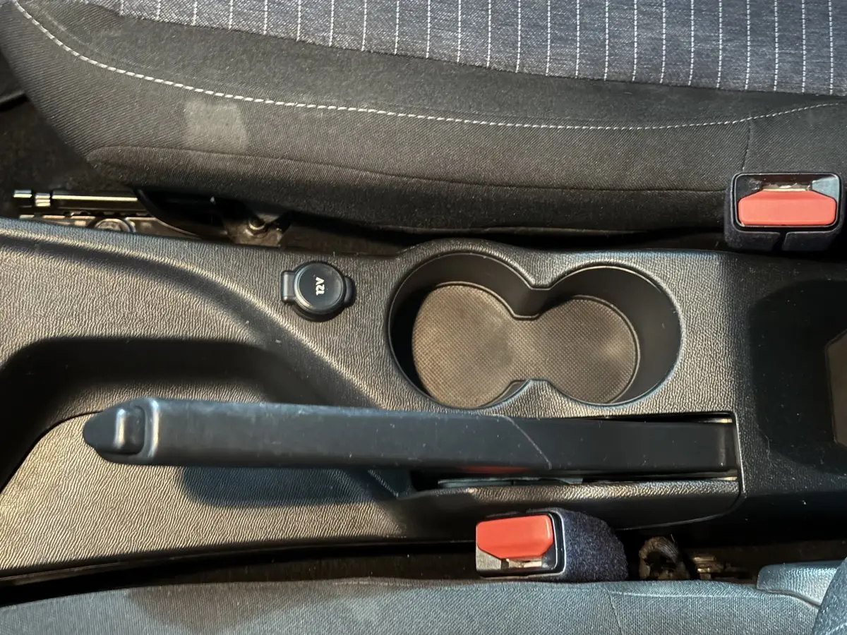 Vue rapprochée de la console centrale noire avec frein à main, prise 12V et porte-gobelets dans une Peugeot 208 blanche.