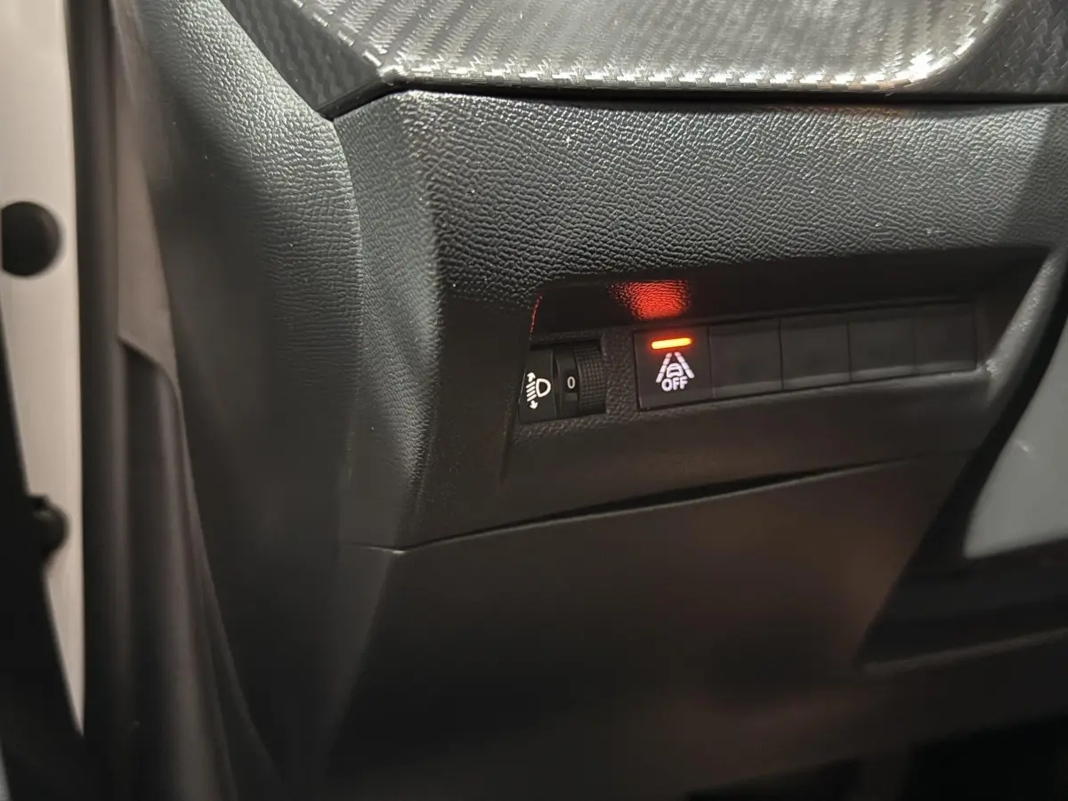 Détail intérieur côté gauche avec bouton d'activation du système d'aide à la conduite sur fond noir, portière blanche visible.