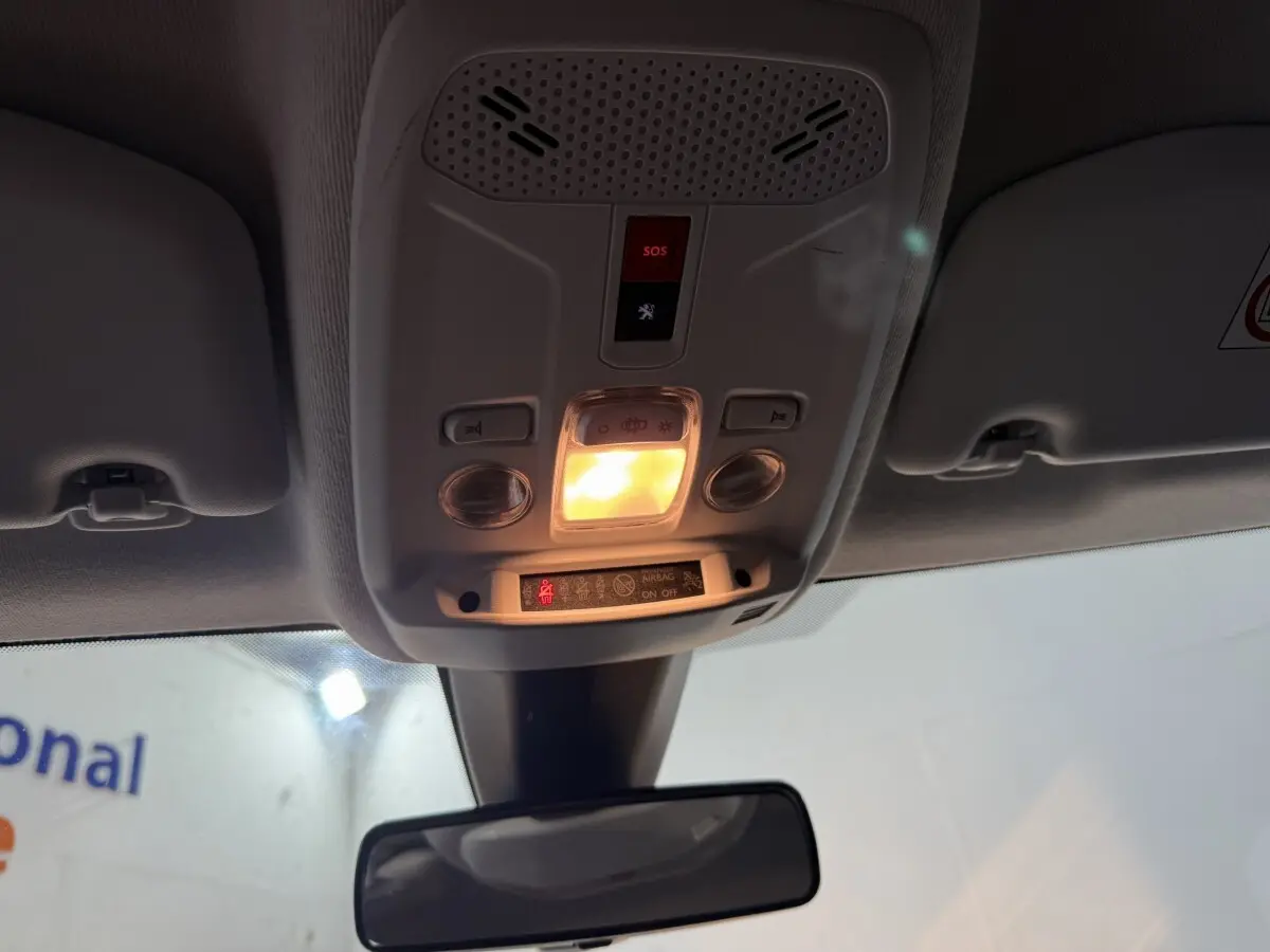Vue intérieure en contre-plongée du plafonnier gris clair avec éclairage et bouton SOS allumé dans une Peugeot 208 blanche.