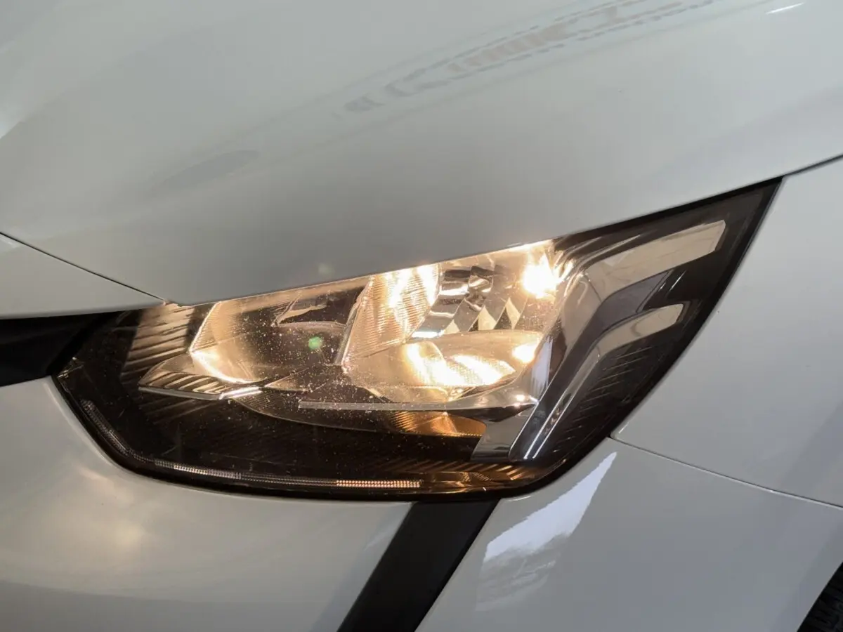 Gros plan sur le phare avant droit allumé d'une Peugeot 208 blanche, soulignant les détails du bloc optique.