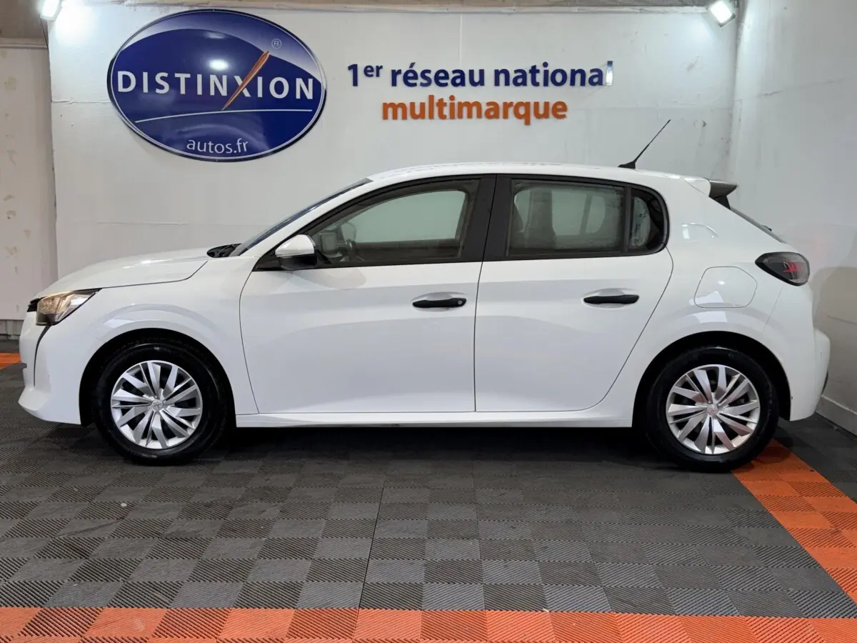 Profil droit d'une Peugeot 208 blanche 2021, compacte avec jantes alliage et feux arrière sombres en intérieur showroom.