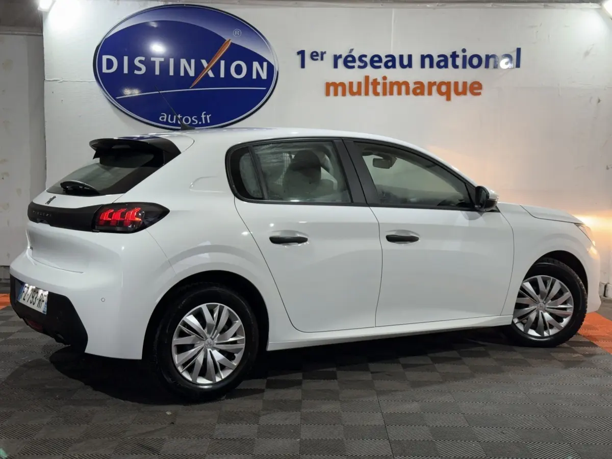 Peugeot 208 blanche vue de profil droit en intérieur, avec feux arrière LED et jantes alliage visibles.