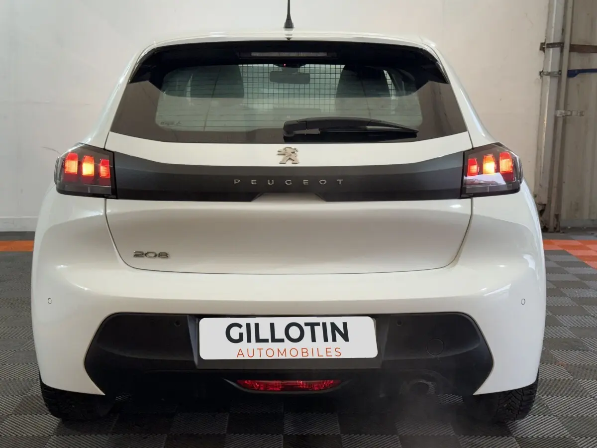 Vue arrière d'une Peugeot 208 blanche de 2021 avec feux LED allumés et logo Peugeot visible sur le hayon.