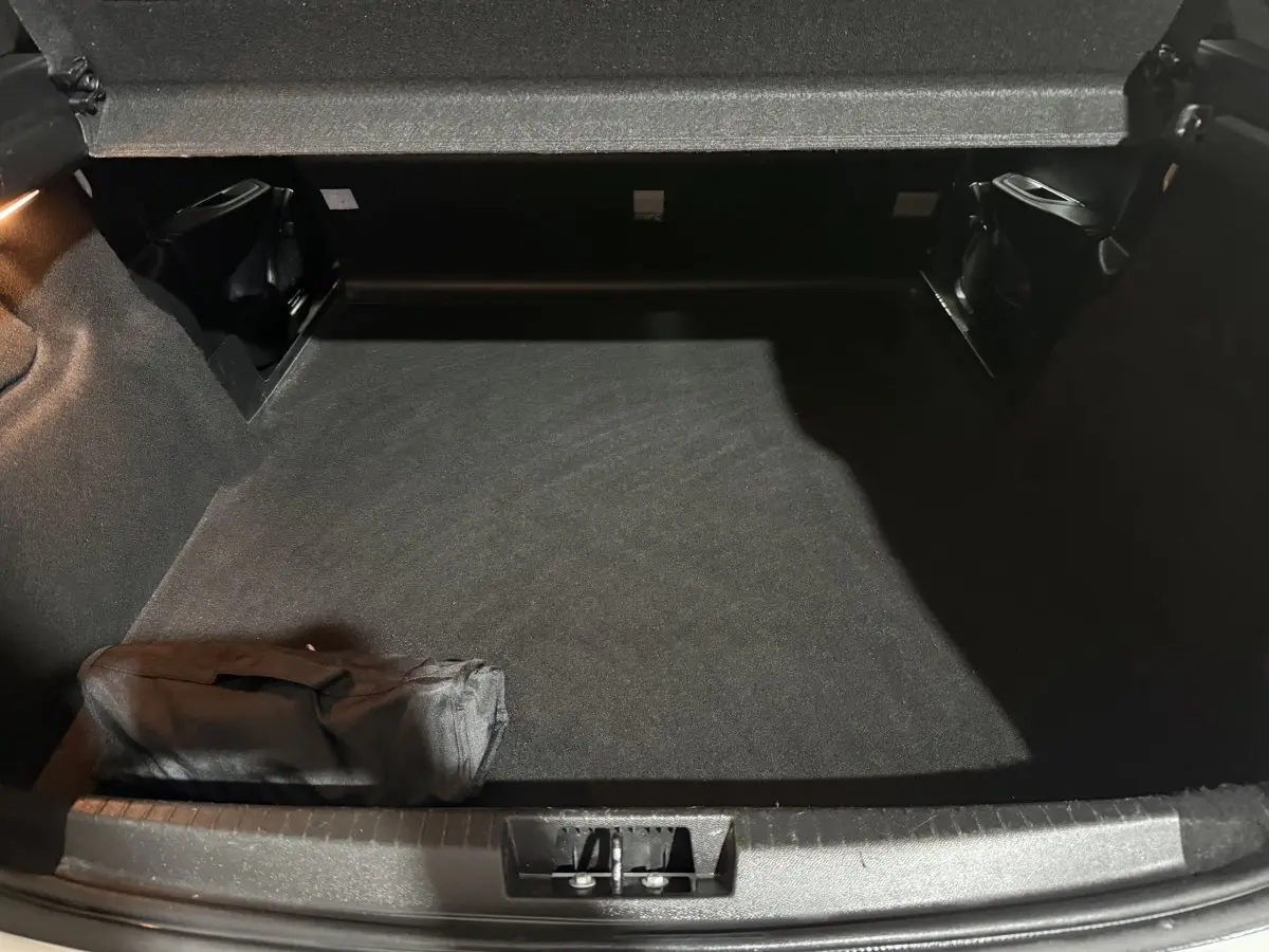 Vue intérieure du coffre spacieux et propre d'une Peugeot 208 blanche, avec un tapis noir et une trousse rangée.