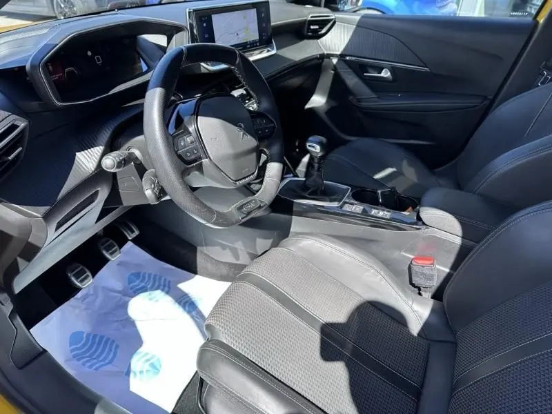 Vue intérieure côté conducteur de la Peugeot 208 GT Line 2020, volant compact, sellerie noire et levier de vitesses manuel.