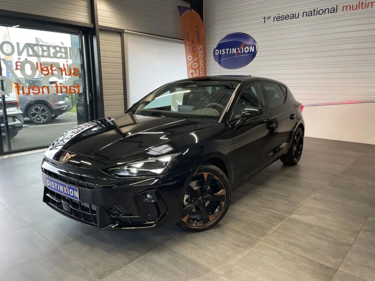 Vue 3/4 avant droite d'une CUPRA Leon noire avec jantes alliage cuivrées dans un showroom intérieur.