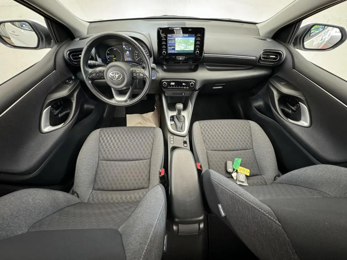 Vue intérieure avant de la Toyota Yaris hybride 2022, tableau de bord noir avec écran tactile central et sièges gris tissu.