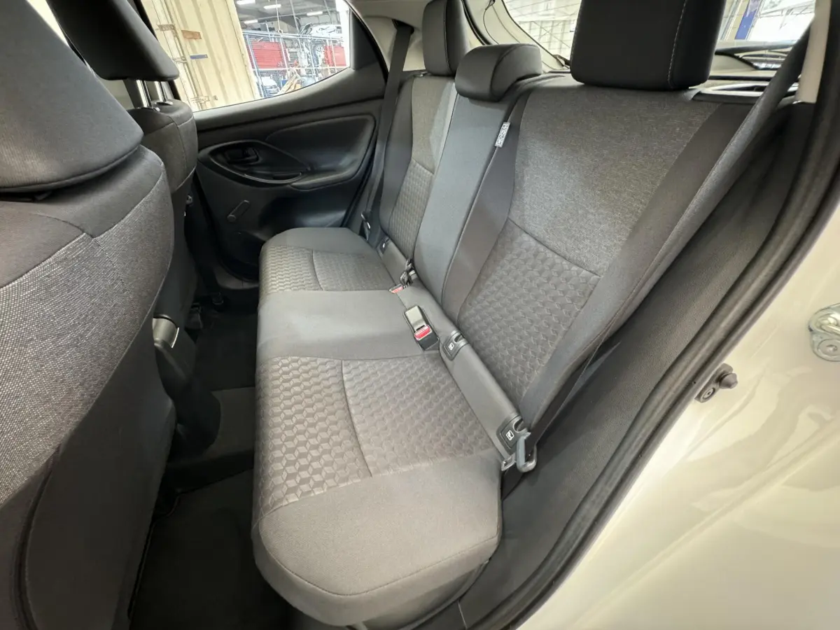 Vue intérieure côté droit sur la banquette arrière grise de la Toyota Yaris hybride blanche 2022 avec portes ouvertes.
